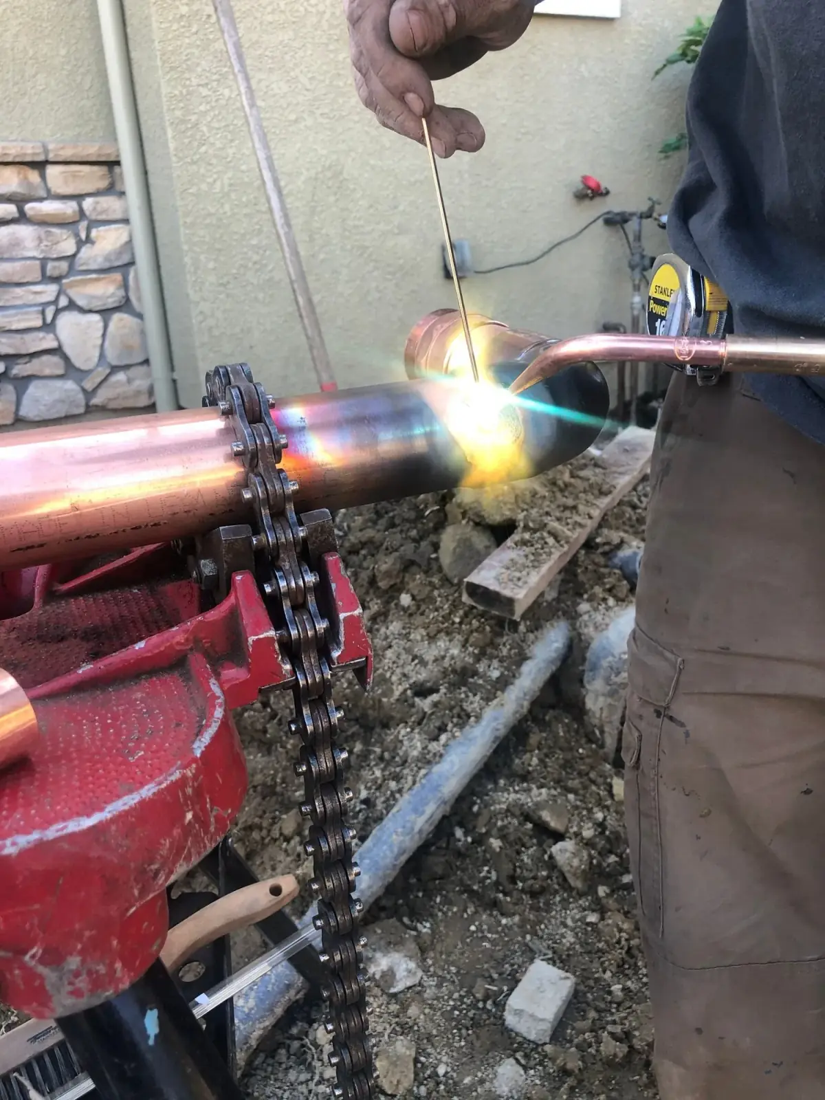 Plumber brazing a copper pipe fitting held in a chain vise